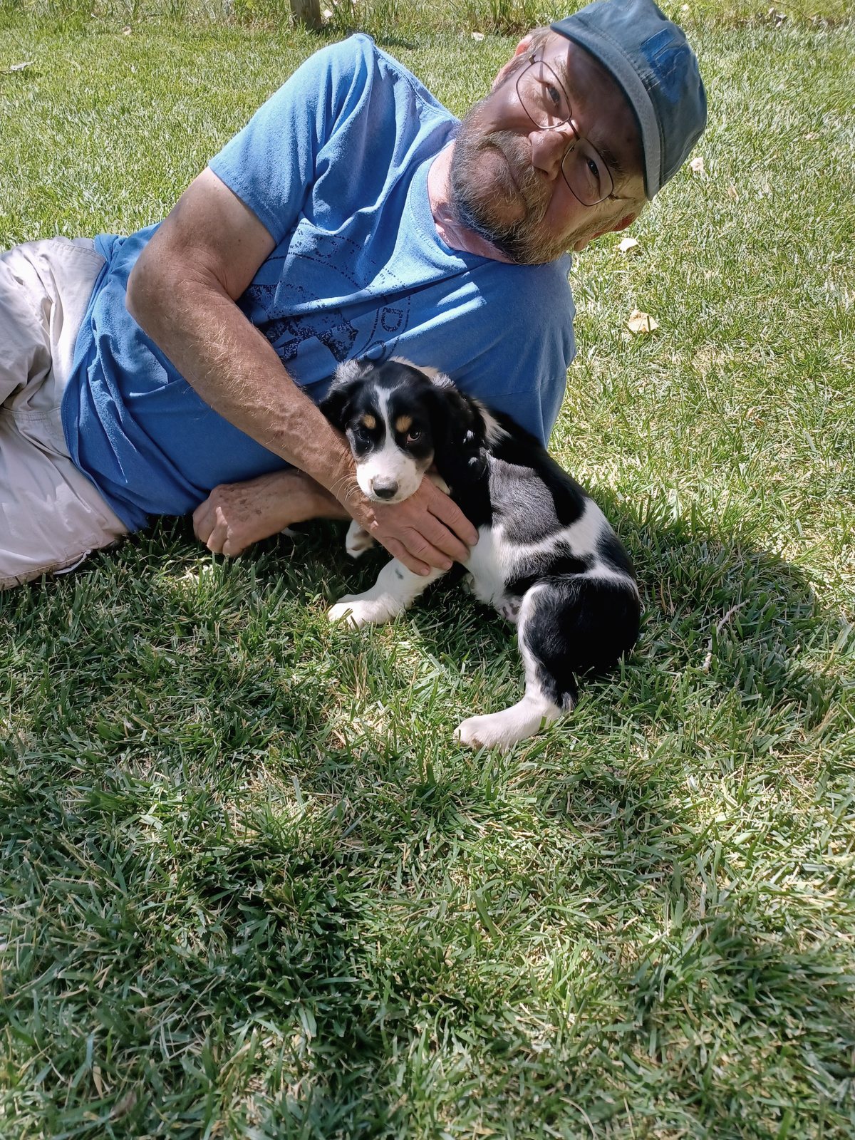 Bob lying on a lawn holding the puppy close to his face