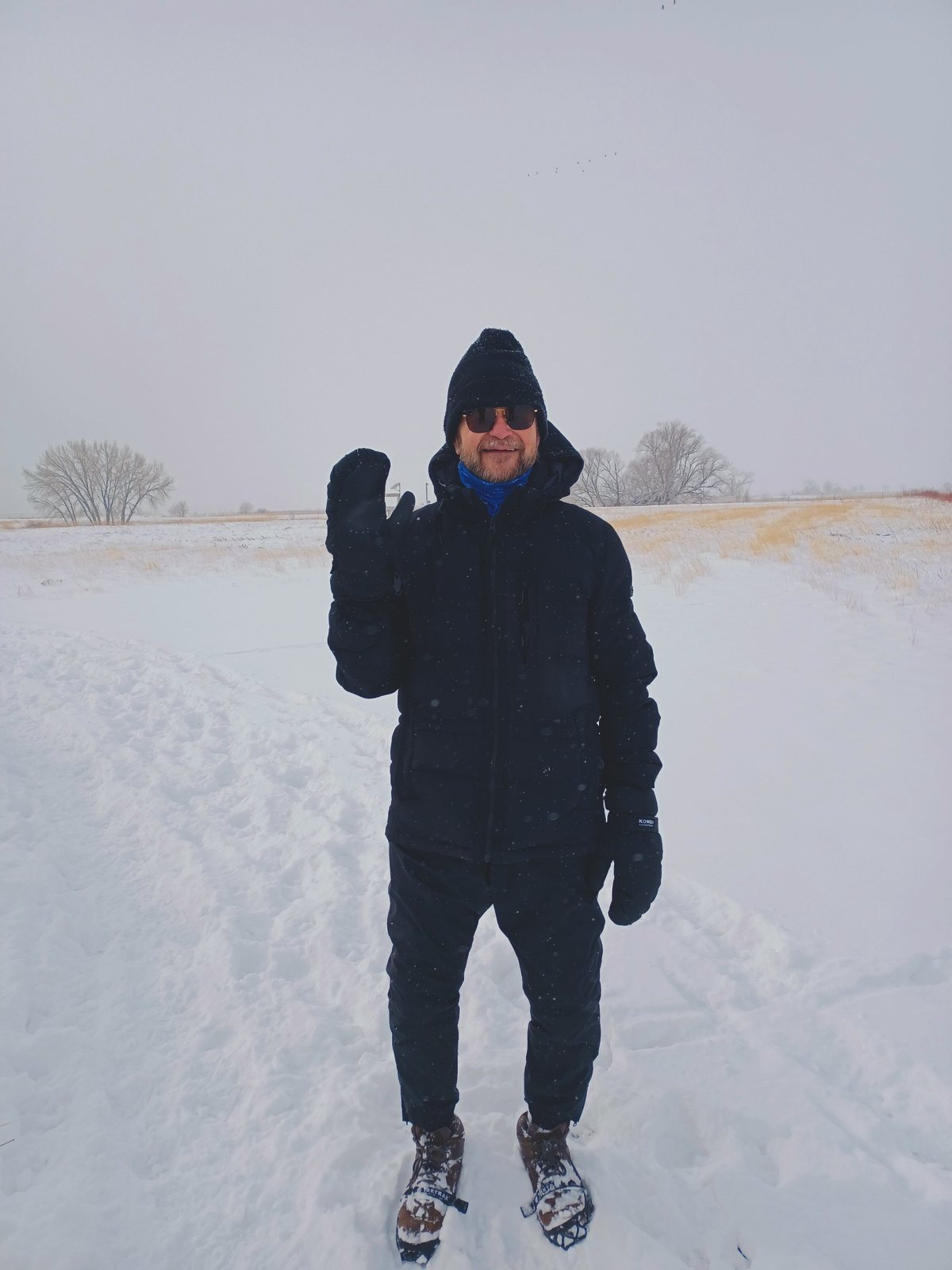 Bob standing alone in deep snow in a whiteout, wearing snowshoes and waving
